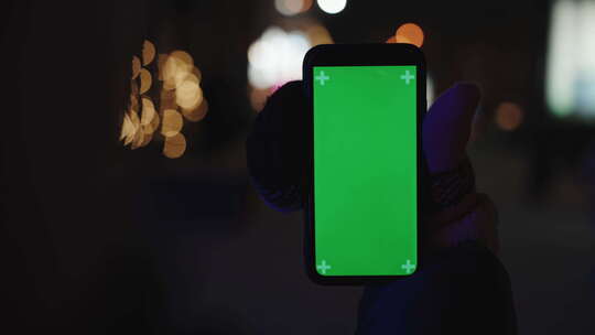 夜间散景背景上手持绿屏的智能手机