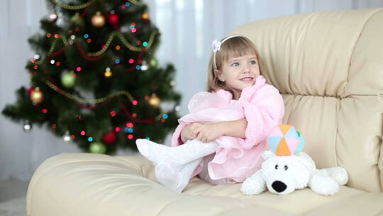 小女孩坐在圣诞树旁边的沙发上