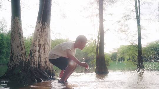 小男孩在树林的池塘边玩水用手泼水4k慢镜头