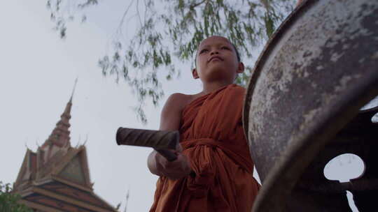 柬埔寨农村寺庙的小和尚在敲钟