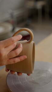 工匠将把手连接到手工粘土杯，背景是模糊的