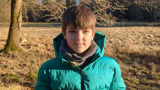 男孩站在丹麦森林的空地上，看着相机
