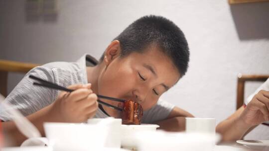 小男孩用筷子夹着红烧肉吃