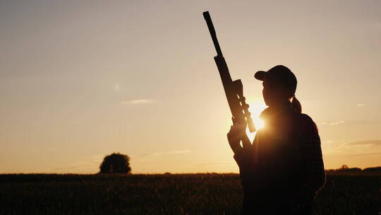 一个拿着狙击枪的女人站在夕阳下的剪影