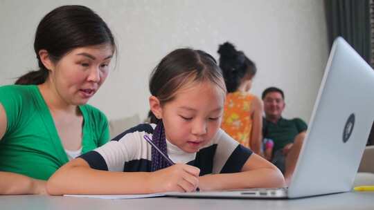 一位亚洲妈妈在家帮助女儿女学生在线学习，