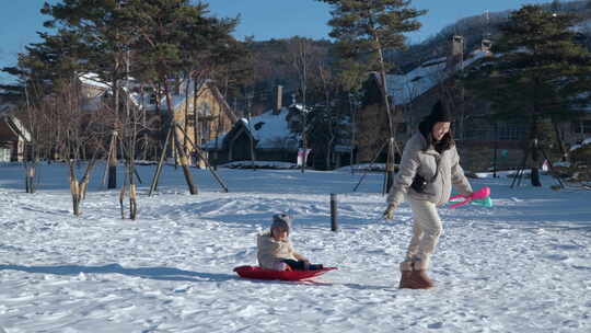 穿着暖冬衣服的母亲在村子里拉着雪橇上可爱