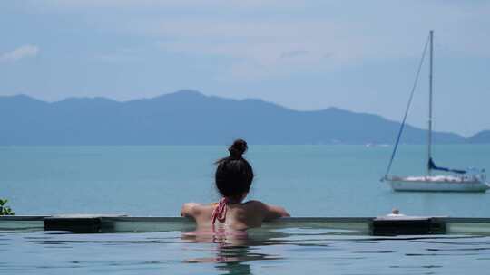 女人在游泳池放松。大海、游艇和山脉背景