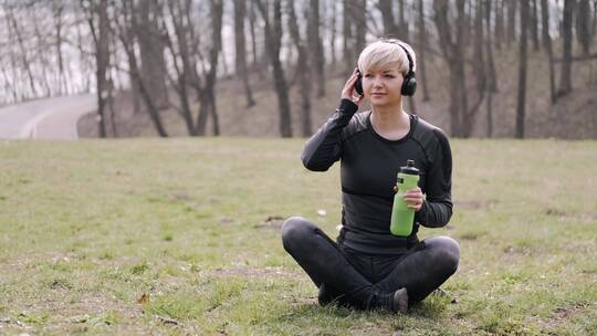 女人坐在草地上听音乐喝饮料