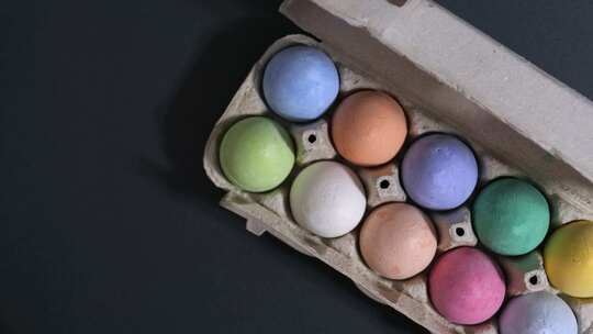 复活节快乐，黑色背景上五颜六色的鸡蛋。一个女人把一盘鸡蛋放在桌子上。