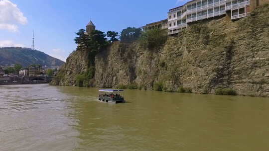 第比利斯库拉河上漂浮的船上的游客，背景是梅特基教堂