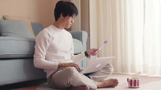 居家男子使用笔记本电脑和手机查看财务报表