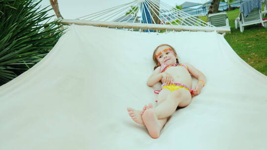 小女孩穿着泳衣在海滩吊床上晒日光浴