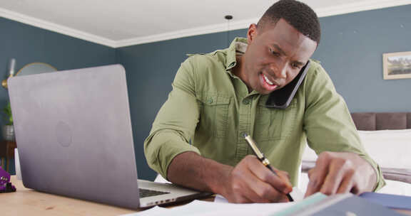 非裔美国男子使用笔记本电脑、说话智能手机和写笔记的视频，在卧室工作