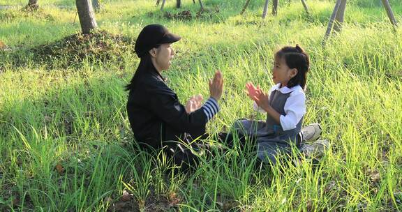 妈妈与女儿坐在阳光草地上拍手玩耍