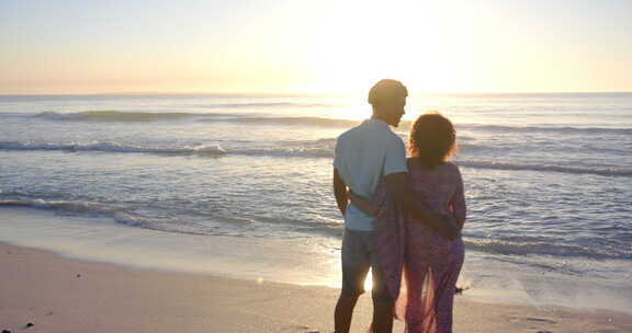出生夫妇拥抱，剪影在海滩日落与复制空间