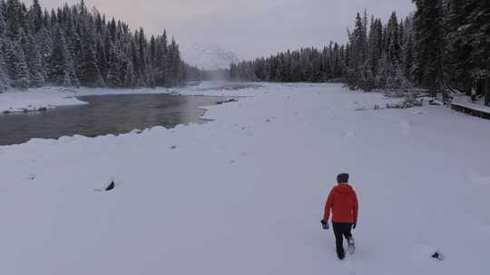 航拍男人艰难地走在新疆喀纳斯河边的雪地里