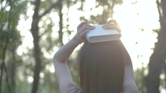 树林中女孩把书挡在头上感受阳光视频素材