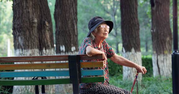 老年人手拄着拐棍孤独的坐在公园长椅上