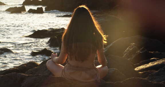 年轻女孩在日落时分在放松的海浪前冥想，静