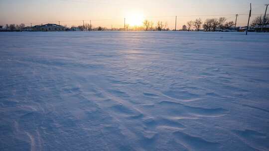 夕阳下的雪地及周边房屋树木景象