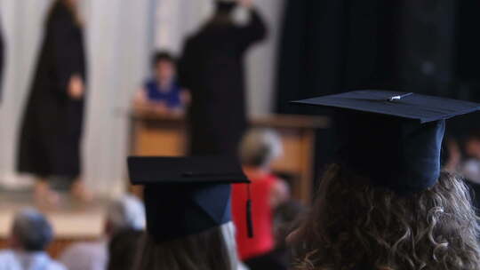 戴帽子、穿长袍的快乐学生观看毕业典礼，领