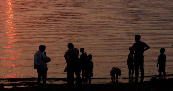 夕阳下傍晚水面波光粼粼游玩的人们
