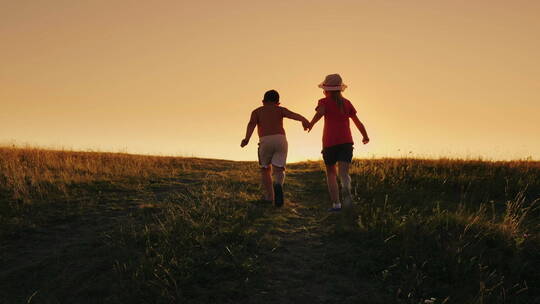 夕阳下男孩和女孩牵手在田野奔跑