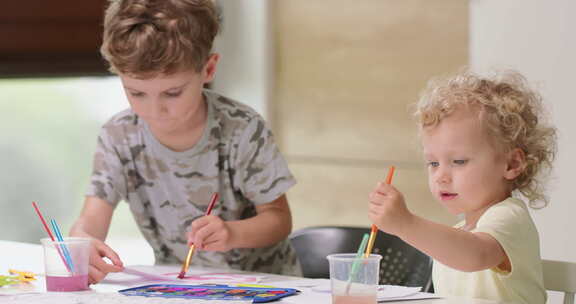 兄弟姐妹坐在桌旁画水彩画女孩试图浸泡画笔