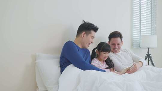 两个男人和一个小女孩在床上玩平板