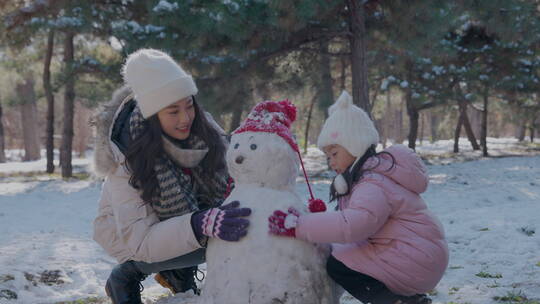 年轻妈妈和女儿在雪地里堆雪人