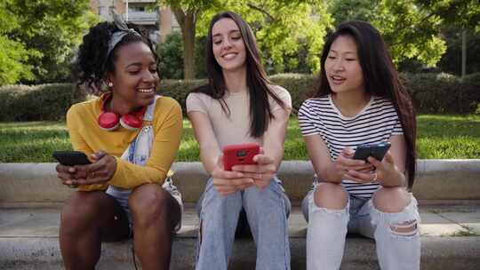 三个快乐的多种族女性在夏季使用电话坐在户