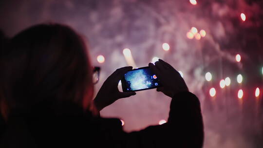 夜晚女人使用手机拍摄烟花