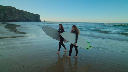 女孩们拿着冲浪板行走在沙滩上