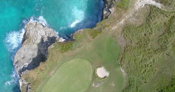 岩石海岸线的自上而下视图，绿松石清澈的海水和带沙子的绿色高尔夫球场果岭