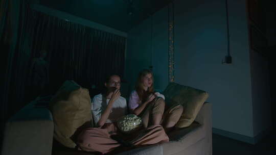 两个女孩坐在家里舒适的沙发上看电视