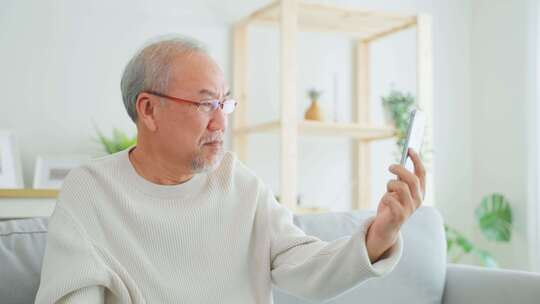 亚洲老年人在客厅使用手机进行视频通话。视频素材模板下载
