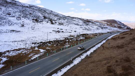 白雪覆盖的山坡下车辆在高原的山路行驶