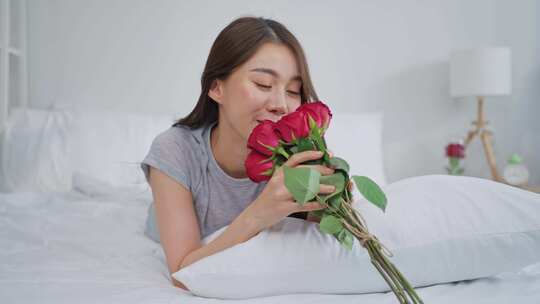 亚洲年轻美女在家卧室看玫瑰花。
