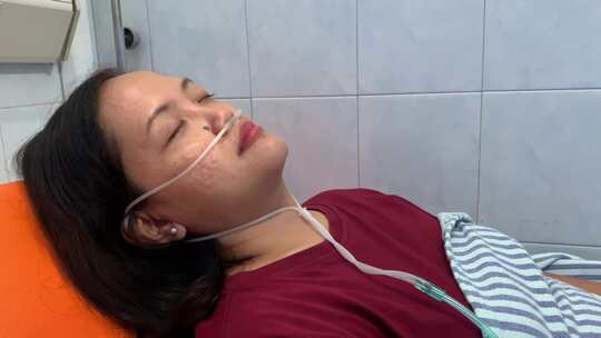 亚洲成年妇女躺在病床上，鼻子里插着呼吸管