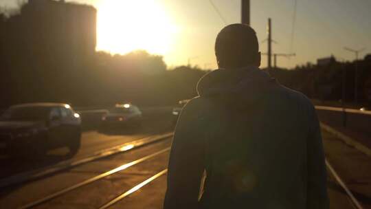 年轻男性在夕阳下穿过电车线。慢动作，跟随