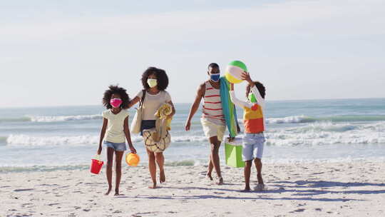 非洲裔美国父母和他们的孩子戴着口罩，在海滩上携带海滩设备