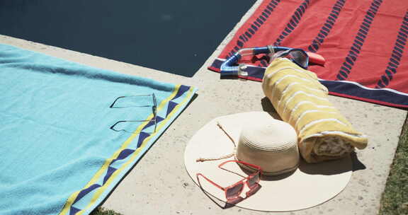 太阳镜、帽子和毛巾在游泳池旁边，暗示着悠