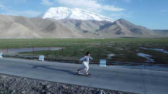 女孩在雪山脚下的公路玩滑板