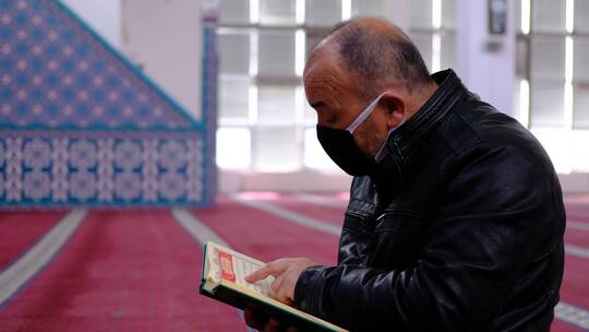 老人戴着面具在清真寺阅读古兰经