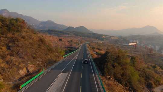 迎着朝霞在空旷山路上行驶的汽车