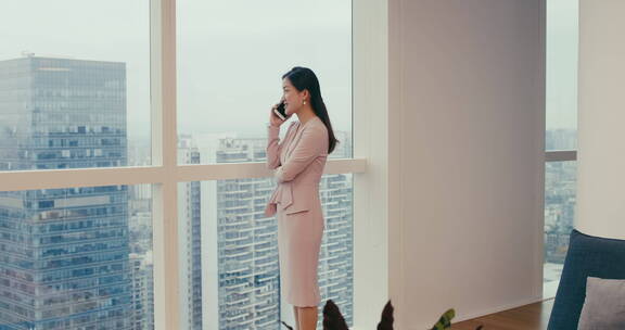 职业女性企业家站在办公室玻璃窗边打电话
