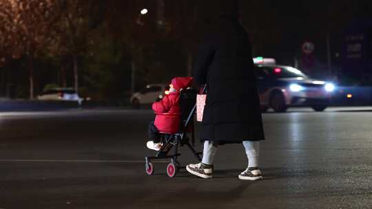 夜晚城市道路上推童车带孩子回家的行人