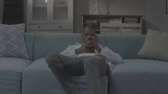 非州男人坐在沙发上玩手机视频聊天葛优躺