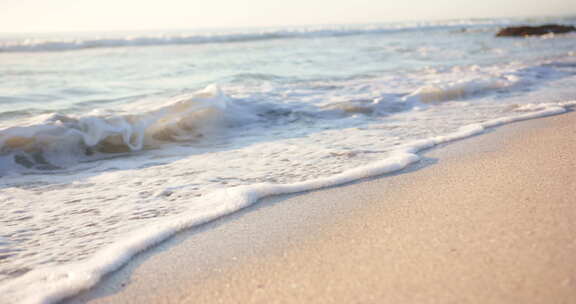 泡沫海浪轻轻亲吻沙滩，阳光反射水面，有复