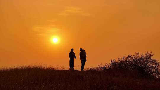 夕阳山坡上欣赏美景的一家人